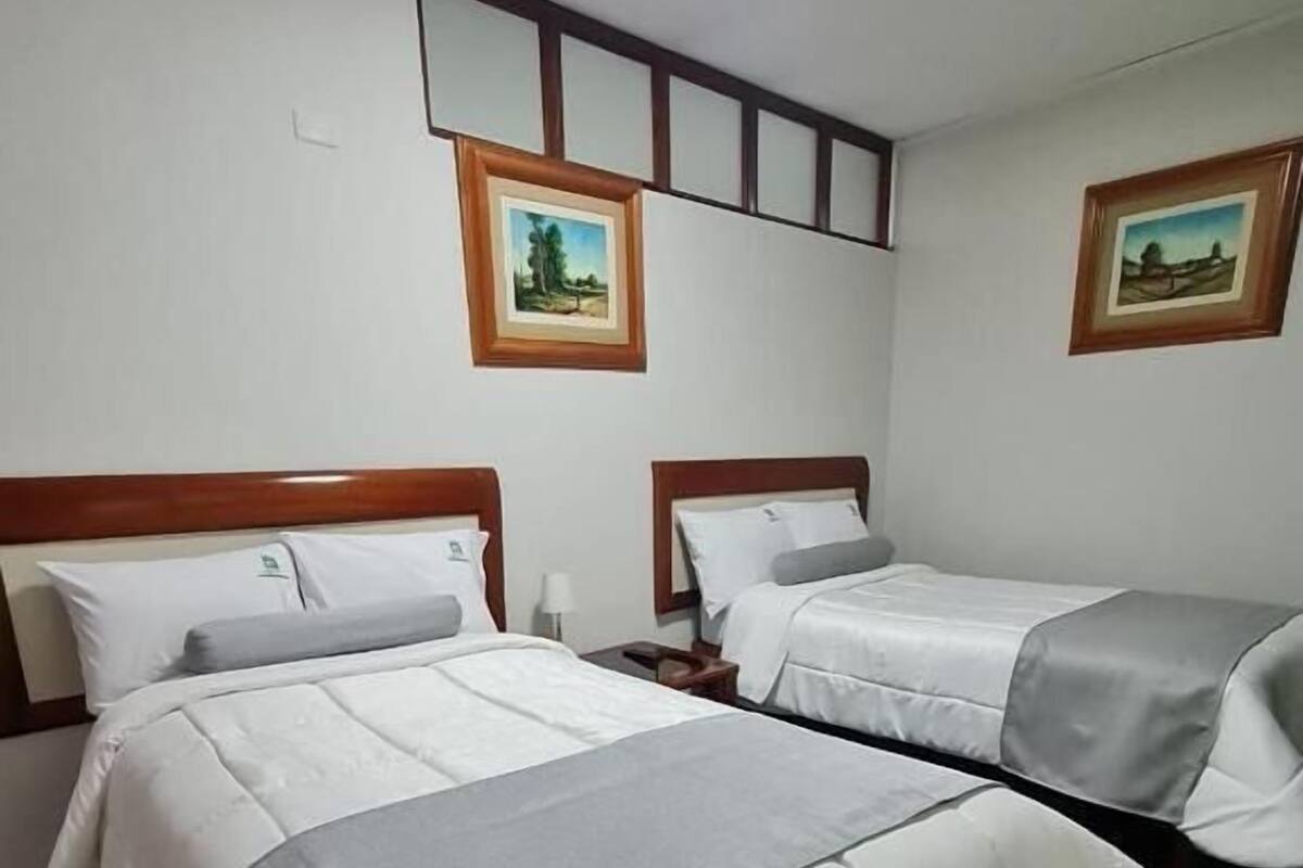 Habitación de hotel con dos camas, una mesita de noche, una lámpara y dos cuadros en la pared.