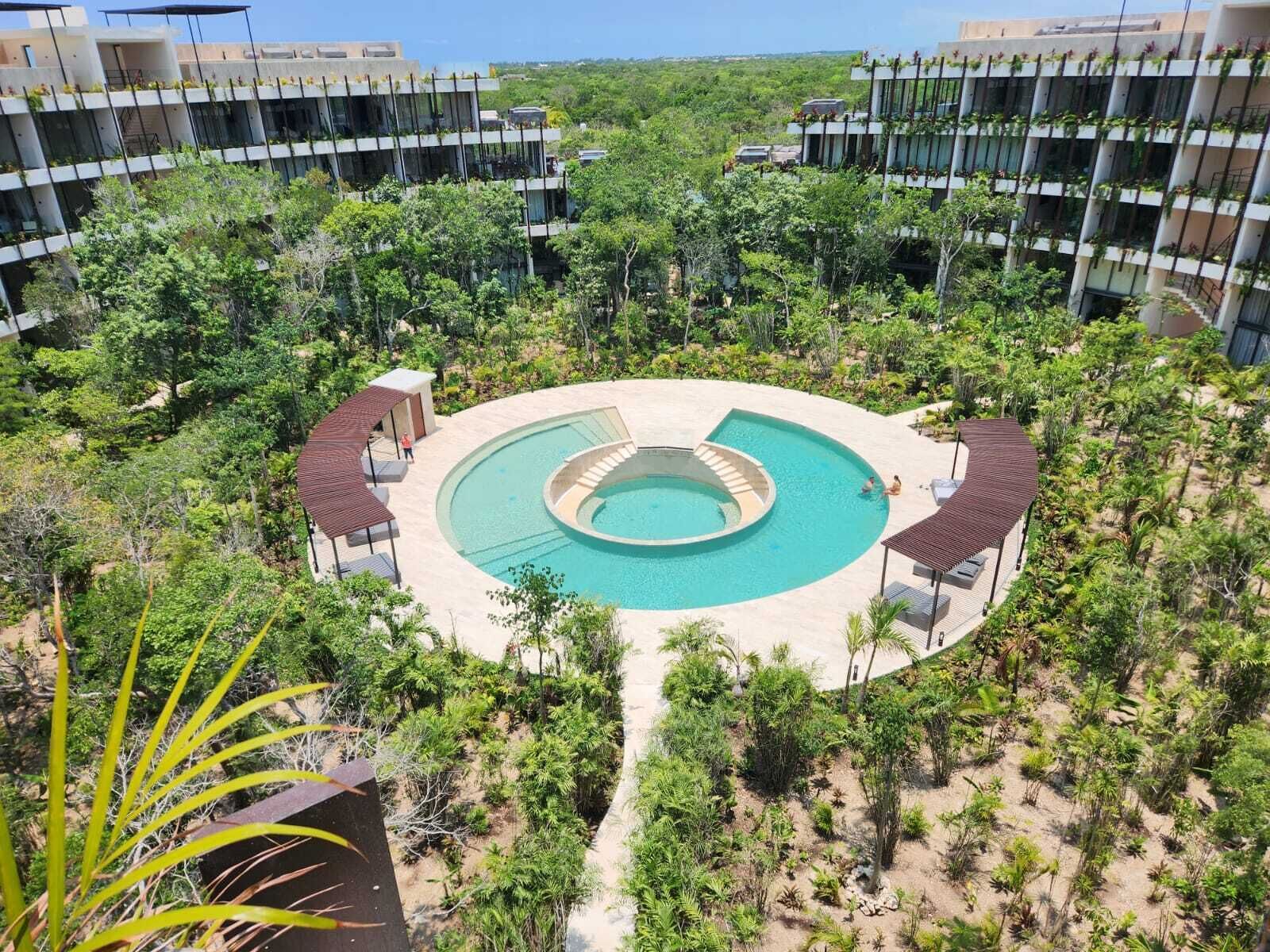 Un complexe hôtelier doté d’une piscine centrale, entouré d’une végétation luxuriante et comprenant plusieurs bâtiments avec des balcons.