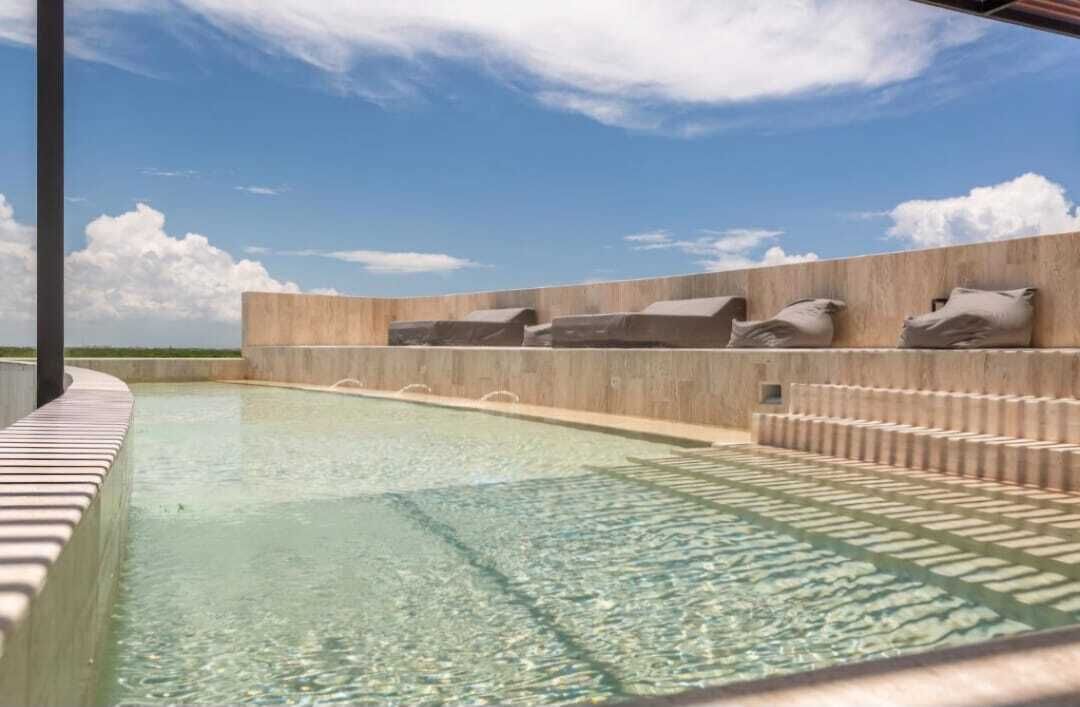Una piscina amb aigua cristal·lina, un videt de rajola i una paret de pedra amb coixins.