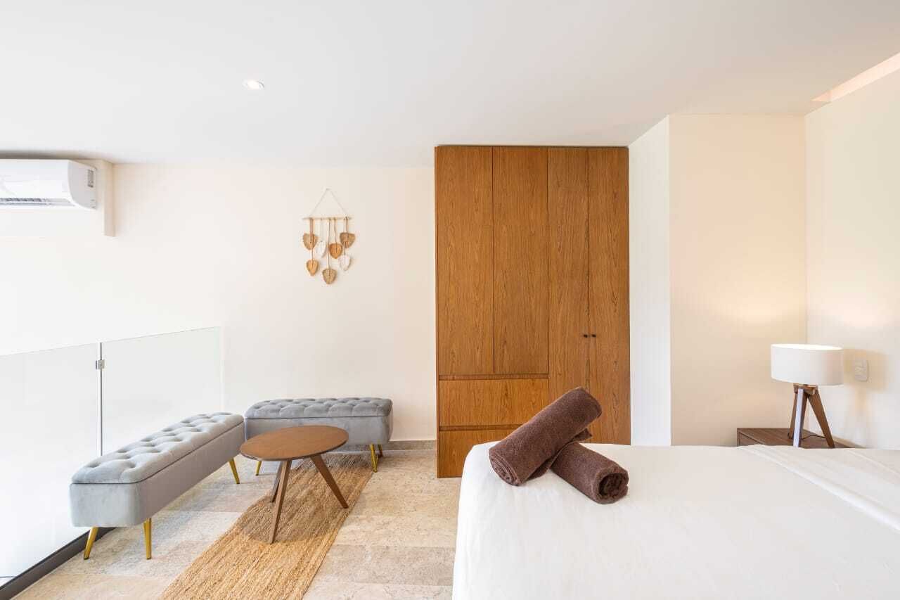 Une chambre d’hôtel moderne avec un lit, un canapé gris, une armoire en bois et une petite table ronde.