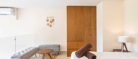 A modern hotel room with a bed, a grey sofa, a wooden wardrobe, and a small round table.