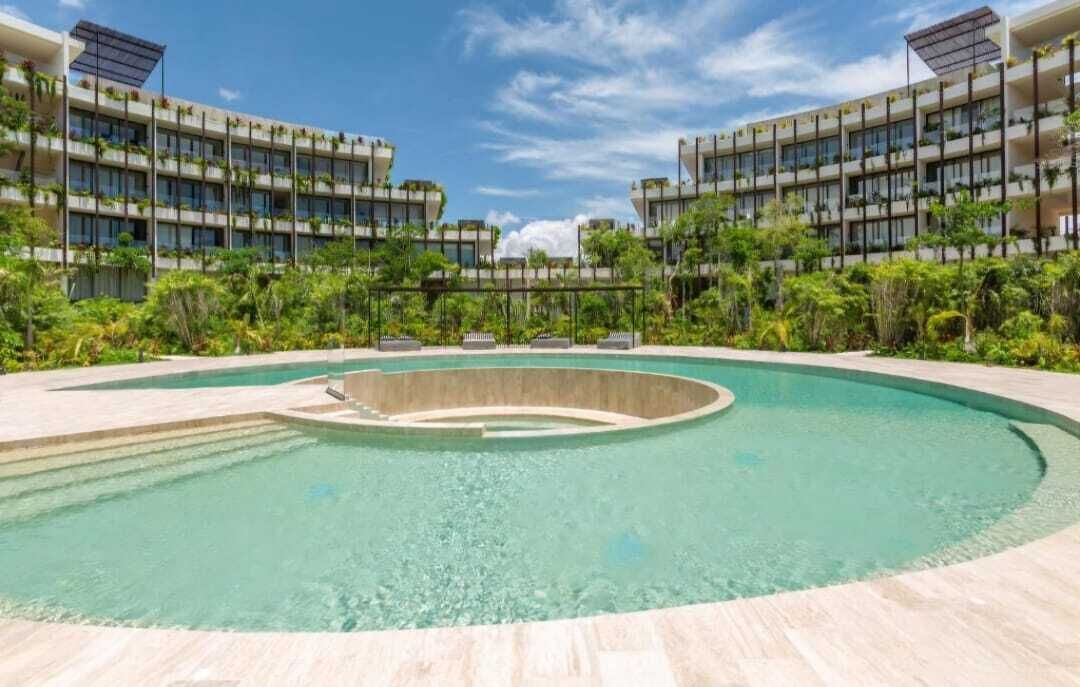 A modern hotel with a central pool, surrounded by lush greenery and multiple floors.