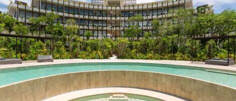 Un hotel moderno con piscina, rodeado de exuberante vegetación y un cielo despejado.
