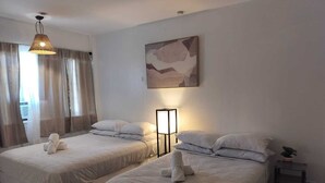 Two beds with white linens, a bedside table with a lamp, and a painting on the wall. - Authentic Stay in Little Havana  6 (Miami)