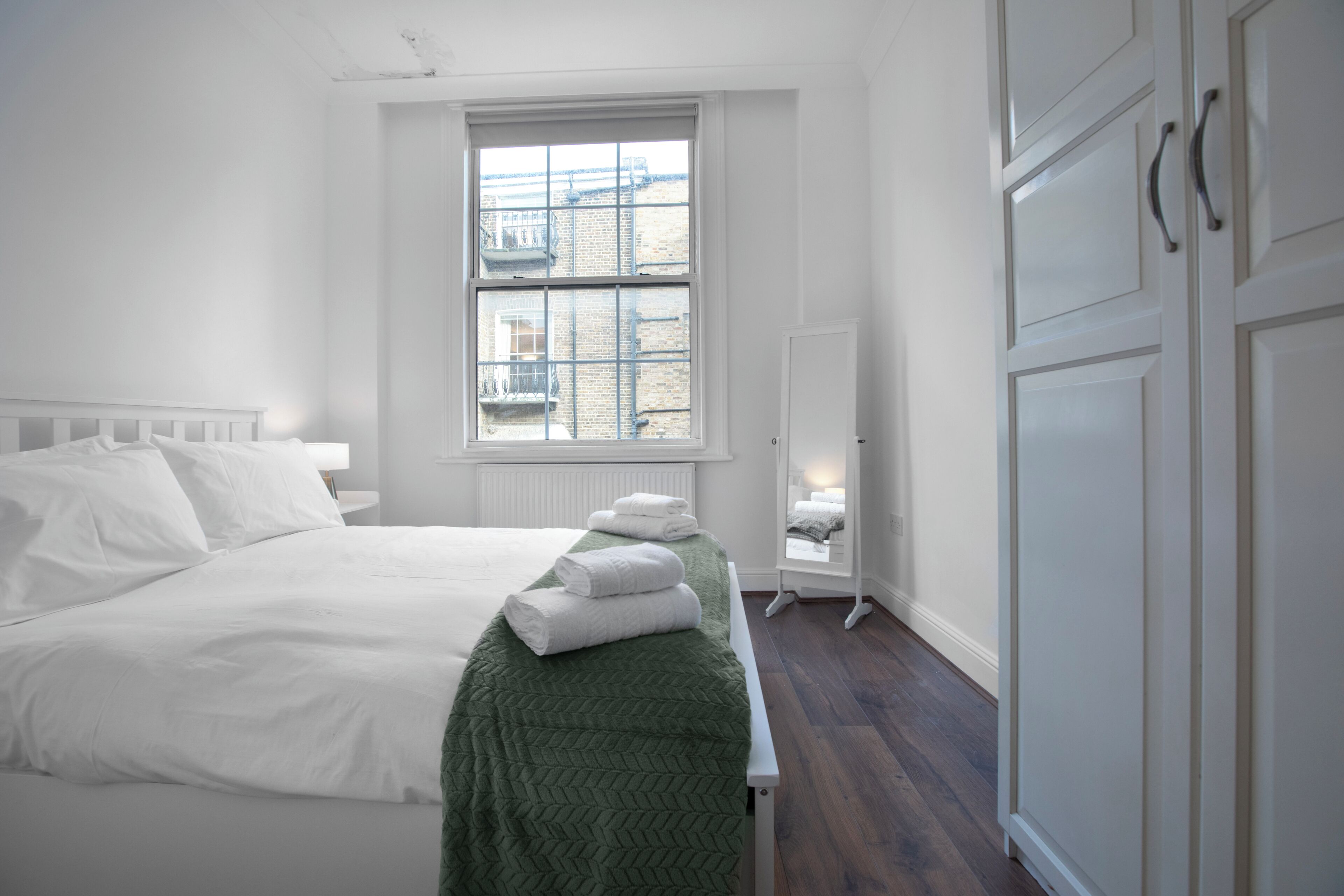 Een slaapkamer met een bed, een raam, een kledingkast en een bankje.