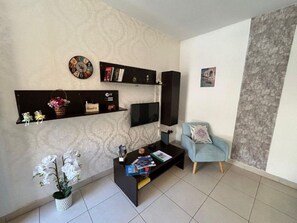 A living room with a flat-screen TV, a sofa, a coffee table, and decorative items. - Modern & Bright Maisonette • Private Terrace • Close to the Sea (Wied il-Għajn)
