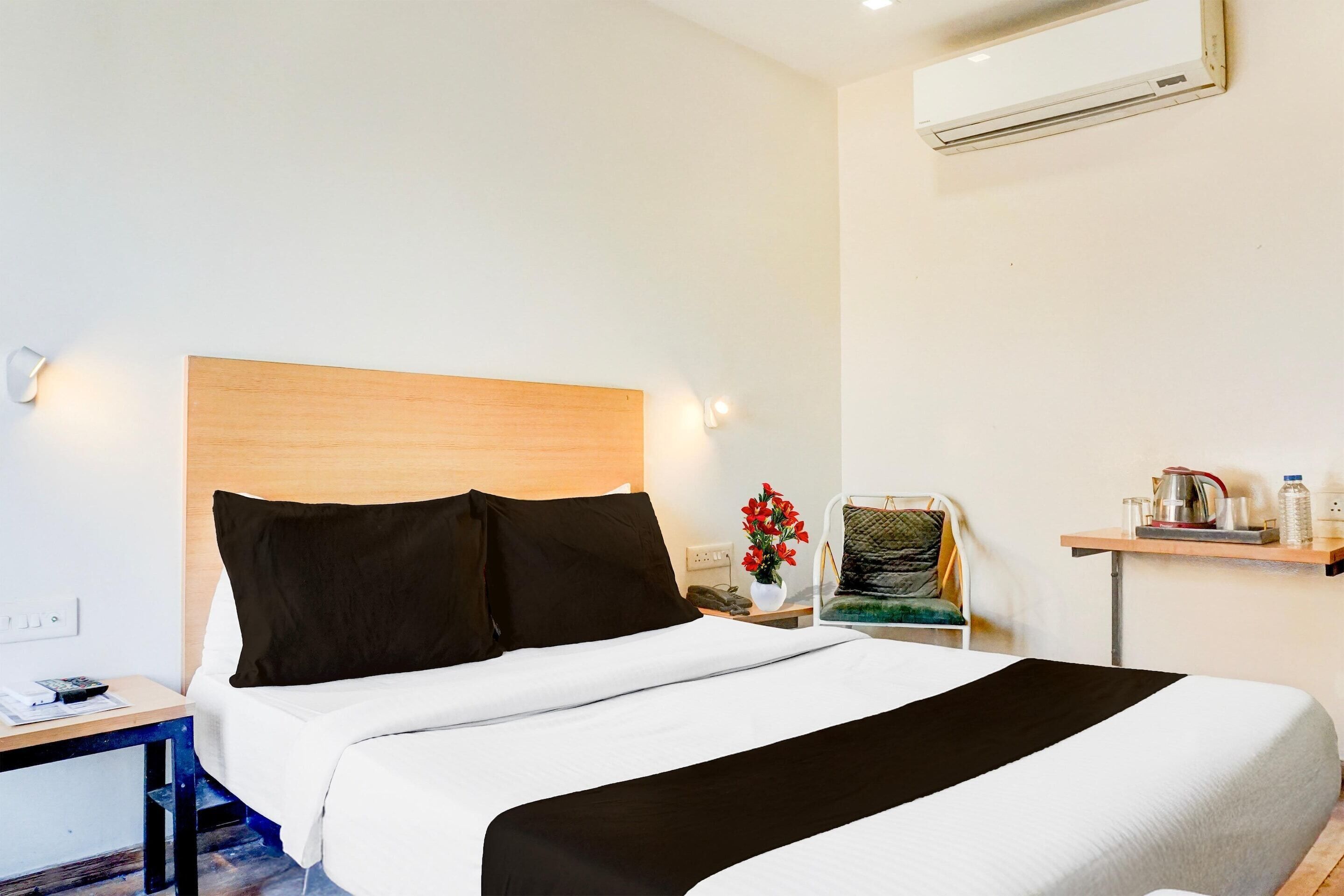 A hotel room with a bed, bedside table, nightstand, chair, and a shelf with items.