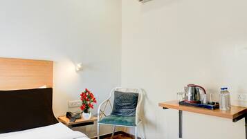 Camera d'albergo con un letto, una sedia, un tavolino con bollitore, bicchieri e una bottiglia d'acqua.