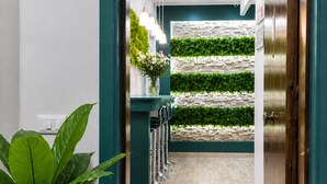 Un couloir avec un mur vert, une plante en pot, une porte et un mur végétal fixé au mur.