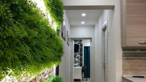 Un couloir avec un mur végétal vertical, une porte donnant sur une pièce et un meuble en bois.