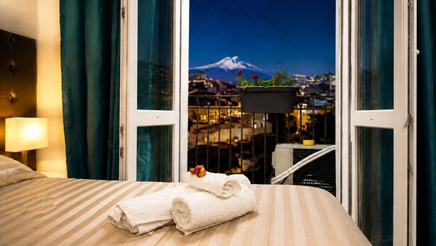 Une chambre d’hôtel avec un lit, une table de chevet, une lampe, une fenêtre avec des rideaux et une vue sur une montagne et le paysage urbain.