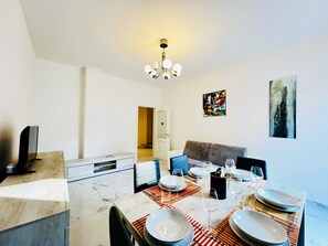 A dining area with a table set for four, a sofa, a television, and artwork on the walls.