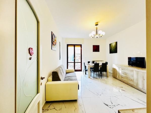 A modern living room with a sofa, dining area, kitchen, and a TV.