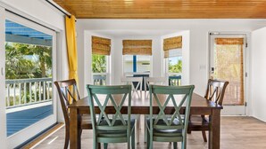 A dining area with a wooden table and chairs, large windows with blinds, and a view of the outdoors. - 🏝️Private Pool + Game Room | Sleeps 15 | Steps to Beach | OWB Beach House (Pensacola Beach)