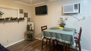 En matplats med ett bord, stolar, en takfläkt, en väggmonterad TV och en luftkonditioneringsanläggning.