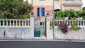 A gated entrance with a staircase leading to a building, surrounded by a white wall with decorative elements and plants.
