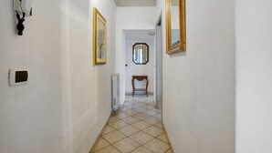 A narrow hallway with white walls, a tiled floor, a radiator, a small table, and two mirrors.