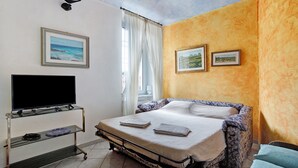 A bedroom with a bed, a television on a stand, and two framed pictures on the wall.