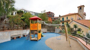 A playground with a slide and a climbing structure, surrounded by buildings and trees.