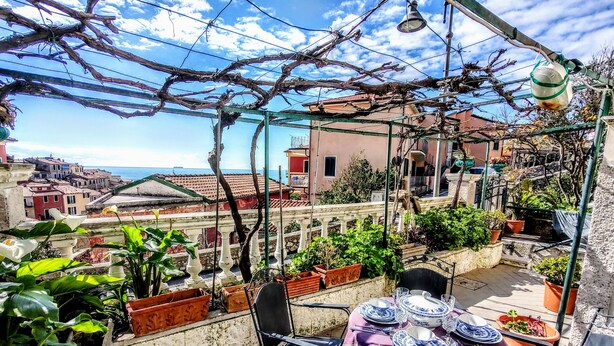 A rooftop terrace with a table set for dining, potted plants, and a view of the cityscape.
