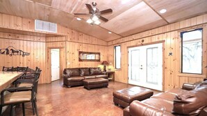 A wooden interior with a dining table, leather sofas, a ceiling fan, and a large window. - Lonestar Lodge in Concan (Concan)