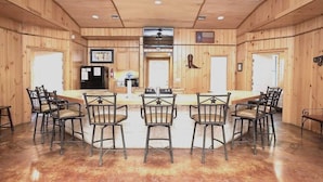 A wooden interior with a central bar area, multiple chairs, and a television mounted on the wall. - Lonestar Lodge in Concan (Concan)