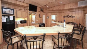 A wooden cabin interior with a kitchen, dining area, and a large island with chairs. - Lonestar Lodge in Concan (Concan)