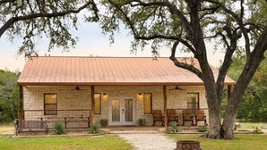 A stone building with a porch, a bench, and a tree in front. - Lonestar Lodge in Concan (Concan)