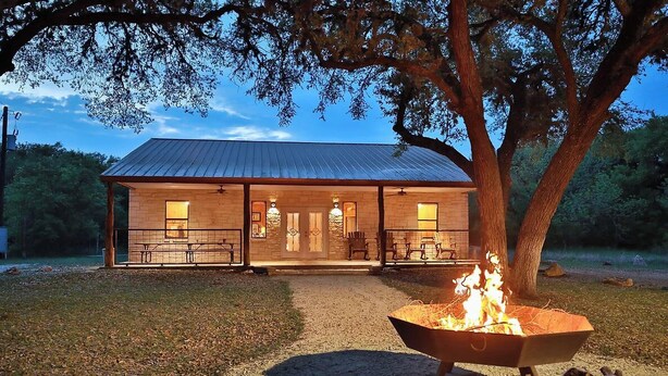 A rustic cabin with a metal roof, a fire pit in front, and a covered porch with seating. - Lonestar Lodge in Concan (Concan)