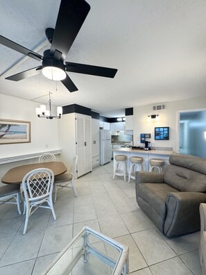 A modern kitchen with white cabinets, a dining area with wicker chairs, a ceiling fan, and a gray sofa. - The Summit Next to Toostie’s – Beachfront Bliss! (Panama City Beach)
