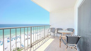 Uma varanda com vista para a praia, duas cadeiras de vime e uma mesa pequena.