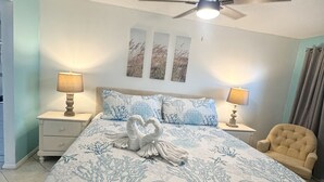 Um quarto com cama, duas mesas de cabeceira com luminárias, um ventilador de teto e uma cadeira.
