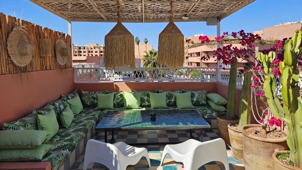 A rooftop terrace with a checkered floor, a sofa set, two white plastic chairs, a table, a woven ceiling, and a cactus plant. - DAR CACTUS-Private House Design-Rooftop-SPA (Marrakech)