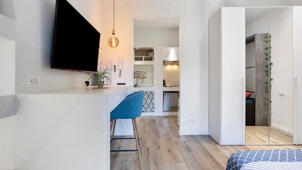 A modern room with a flat-screen TV, a bar area with stools, a bed with patterned bedding, and a kitchen in the background. - La Casa Delle Meraviglie – Porta Romana, Milan (Milano)