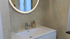 A bathroom with a white sink, a round mirror, and a bottle of soap.