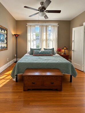 A bedroom with a bed, a ceiling fan, a nightstand, a lamp, a bench, and a door. - Relaxing 2-bedroom 2 bath Retreat in the Heart of New Orleans,  1700 Square Feet (New Orleans)