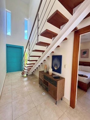 A modern staircase with wooden steps and metal railings, leading to a bedroom with a bed and a blue wall art piece. - 4bd Villa Azure in Oceanfront Comm Sosua Ocean Vil (Sosúa)