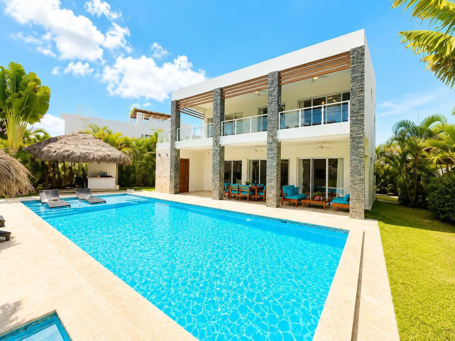 Ein modernes, zweistöckiges Haus mit Swimmingpool, Sitzgelegenheiten im Freien und üppiger Bepflanzung.