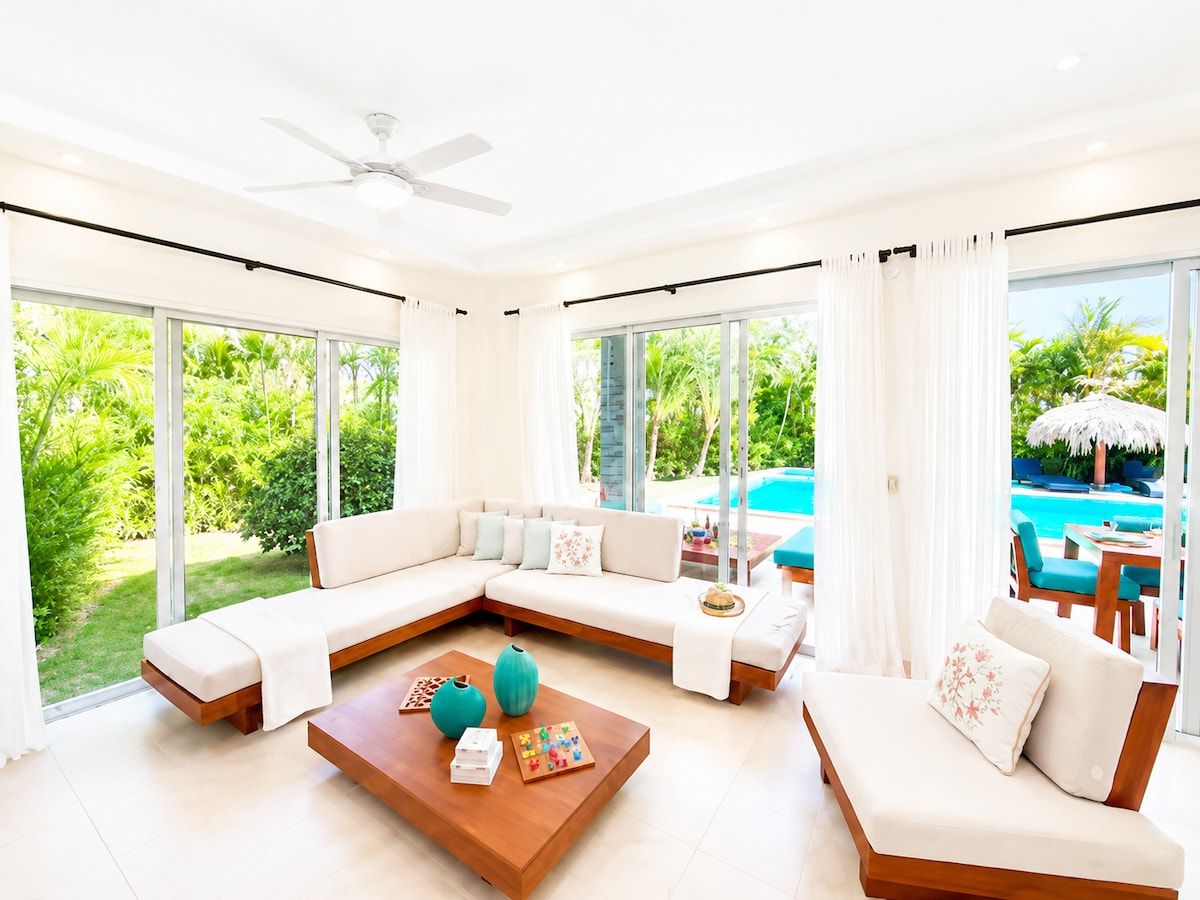 A modern living room with a sectional sofa, a wooden coffee table, and a view of a swimming pool.