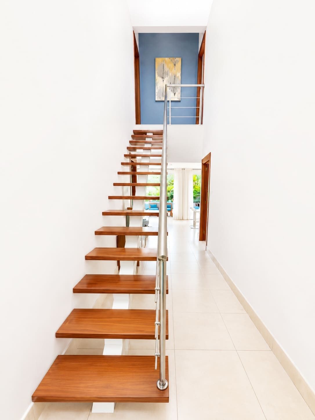 A modern staircase with wooden steps and a metal handrail, leading to a room with a blue accent wall and a painting.