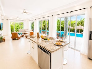 Eine moderne Küche mit Kochinsel, großen Fenstern und Blick auf Pool und Grünflächen.