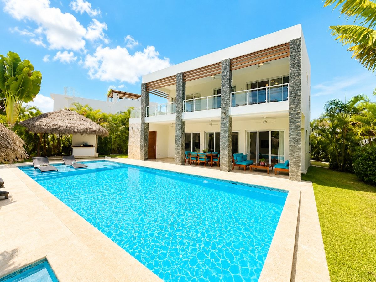 A modern two-story house with a swimming pool, outdoor seating, and lush greenery.