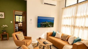 Ein Wohnzimmer mit einer Sofagarnitur, einem Couchtisch und einem an der Wand befestigten Fernseher.