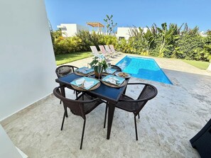 A dining table with chairs, a pool, and a garden view. - 3bd Villa Aura in Oceanfront Comm Sosua Ocean Vill (Sosúa)