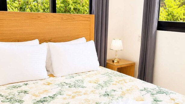 Ein ordentlich bezogenes Bett mit floralem Überwurf, ein Tablett mit Frühstücksangeboten und Blick auf grüne Natur.