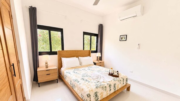 A bedroom with a wooden bed, two bedside tables, a ceiling fan, and a window with curtains. - 3BD Villa in SOV | Private Pool & Peaceful Retreat (Sosúa)