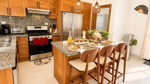 A modern kitchen with wooden cabinets, stainless steel appliances, a granite countertop, and a central island with bar stools. - 3BD Villa in SOV | Private Pool & Peaceful Retreat (Sosúa)