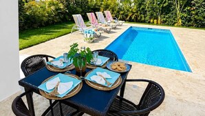 A poolside dining area with a table set for four, surrounded by lounge chairs and a pool. - 3BD Villa in SOV | Private Pool & Peaceful Retreat (Sosúa)