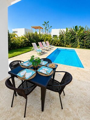 A poolside dining area with a table set for four, surrounded by lounge chairs and a pool. - 3BD Villa in SOV | Private Pool & Peaceful Retreat (Sosúa)