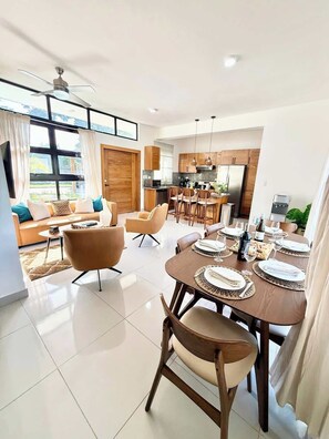 A modern living room with a sofa, armchairs, a dining table set for six, and a kitchen in the background. - 3 bd Villa Solis in Oceanfront Community Santa Fe (Sosúa)